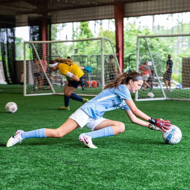Teenagers practicing being soccer goalkeepers. They are training at an indoor/outdoor facility are practicing diving onto the soccer ball. They are wearing EPIC Soccer Academy goalkeeper gloves and are being trained by professional soccer coaches. 